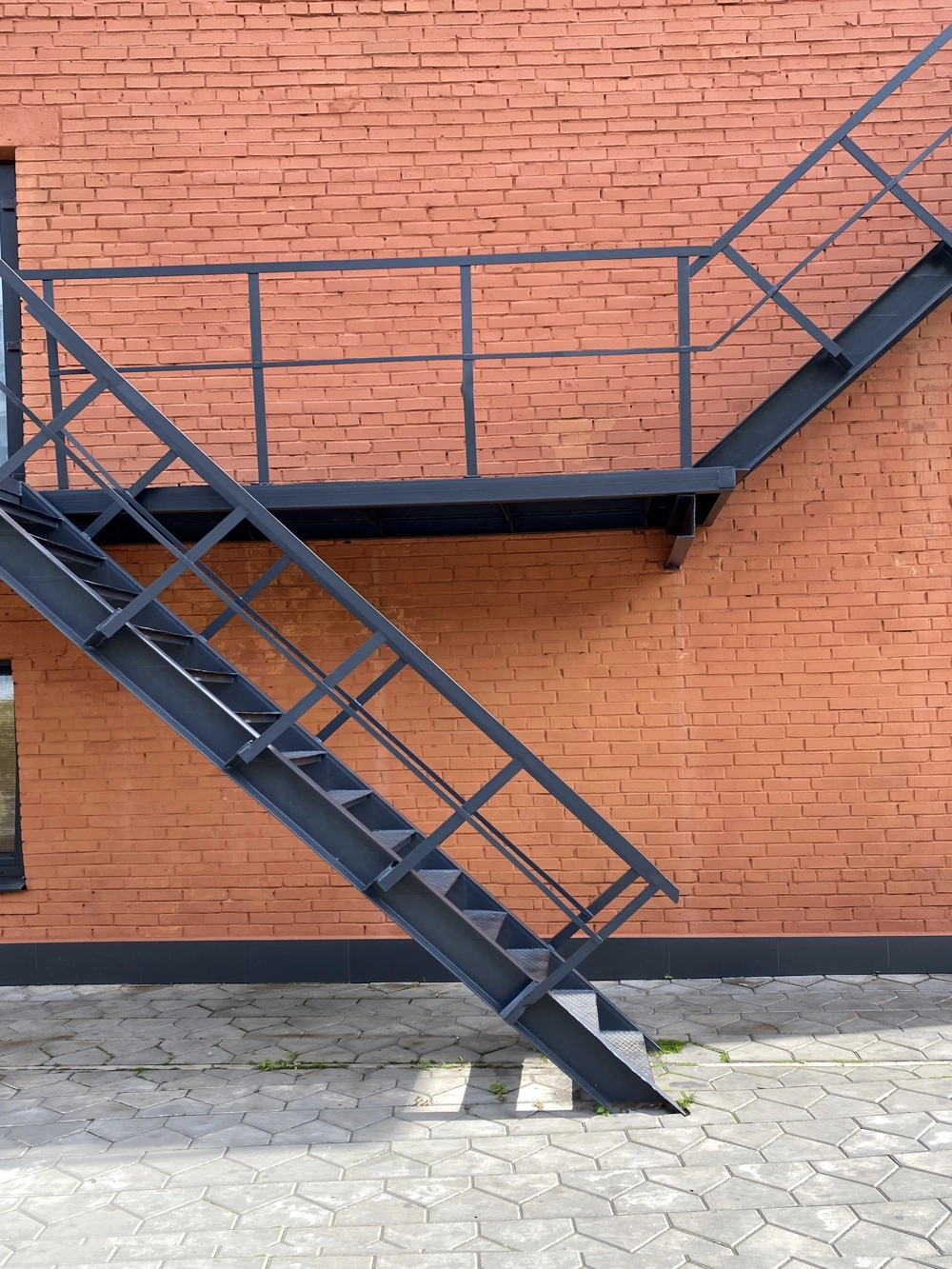 Metalltreppe mit pulverbeschichtetem Metallgeländer und Podest vor roter Backsteinwand