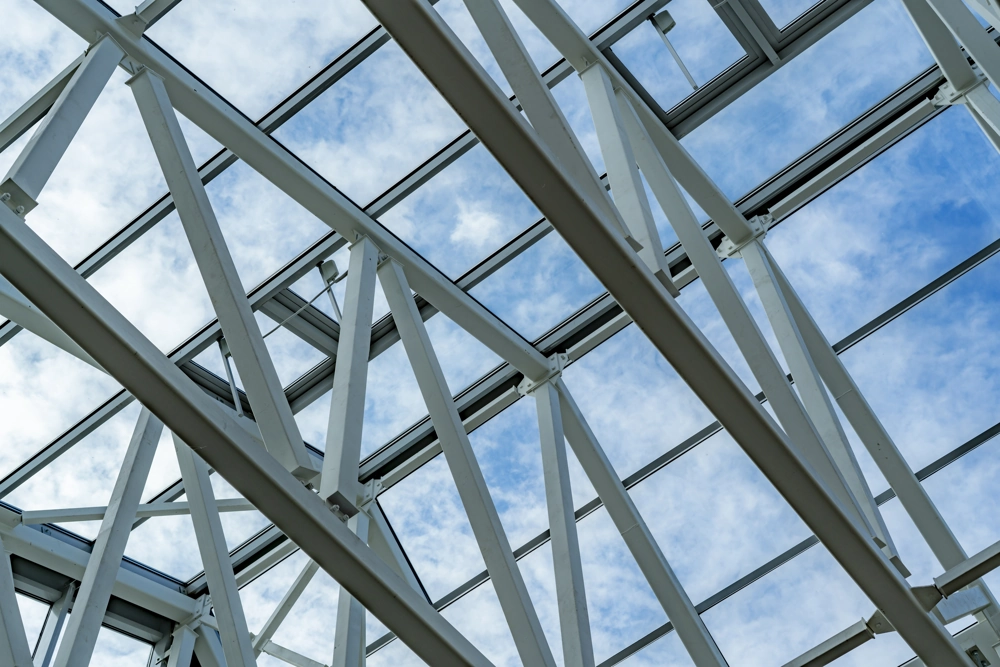Innenaufnahme einer Stahlträgerkonstruktion im Hallenbau mit Glasdach und weißen Profilen