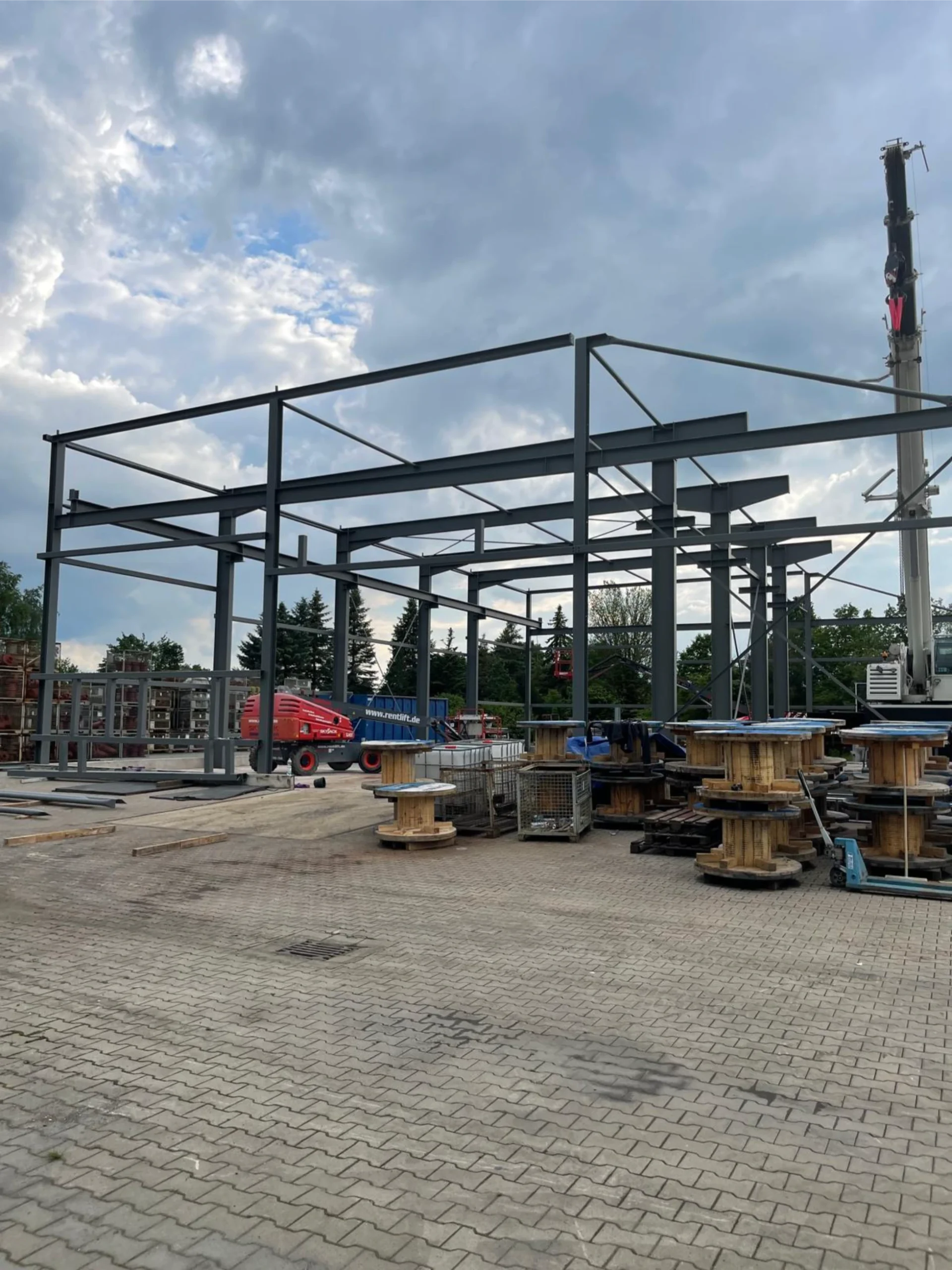 Montage von Stahlkonstruktionen für eine neue Halle auf einer Baustelle mit Kran und Hebebühne.