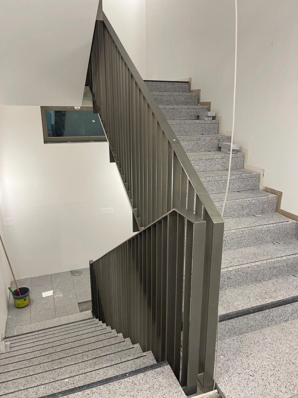 Innenbereich einer Metalltreppe mit Stahlgeländer und grauen Terrazzo-Stufen
