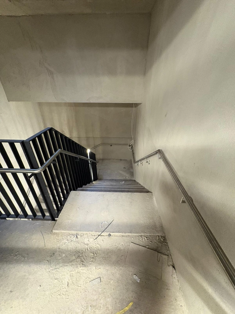 Betontreppe in Rohbau mit schwarzem Treppengeländer und seitlichem Handlauf aus Edelstahl