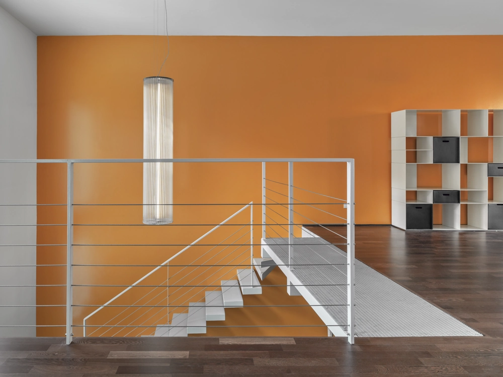 Moderner Innenbereich mit Metalltreppe und filigranem Treppengeländer aus Edelstahl vor oranger Wand