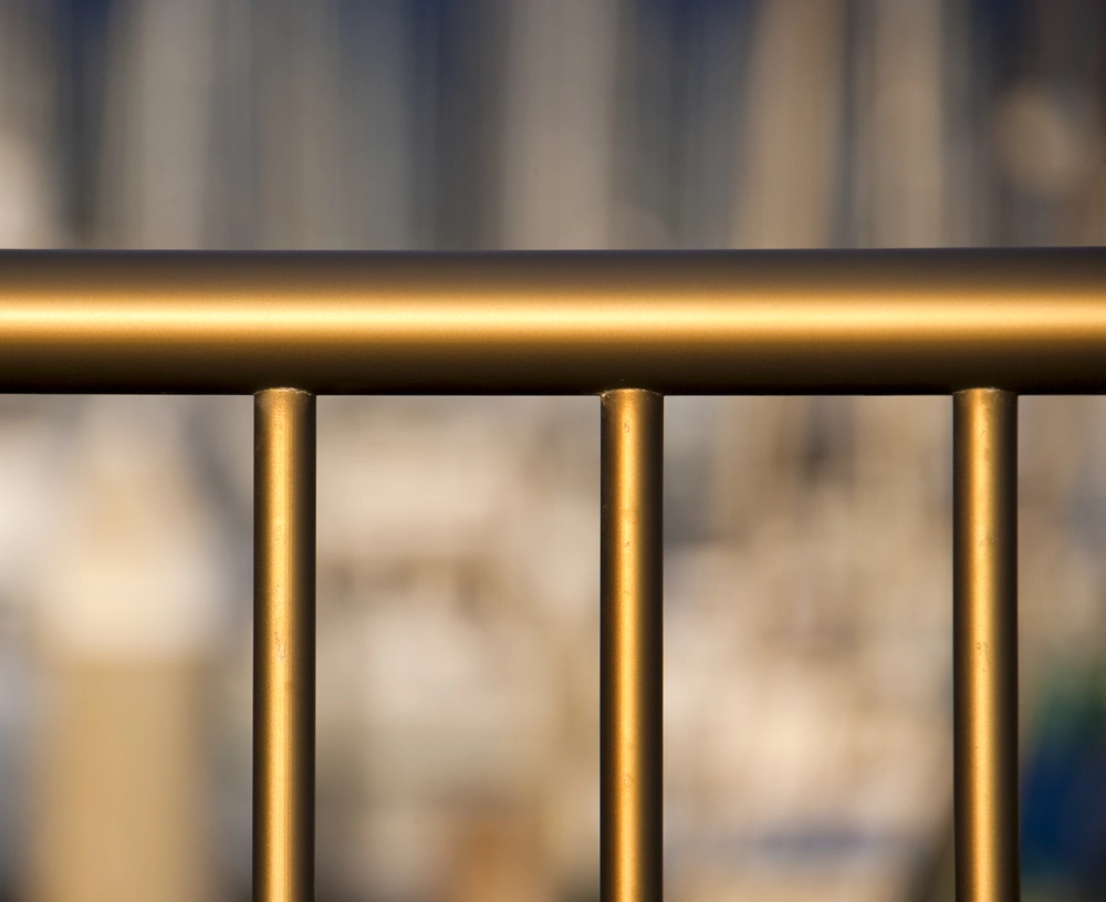 Goldfarbenes Metallgeländer mit rundem Handlauf vor unscharfem Hintergrund