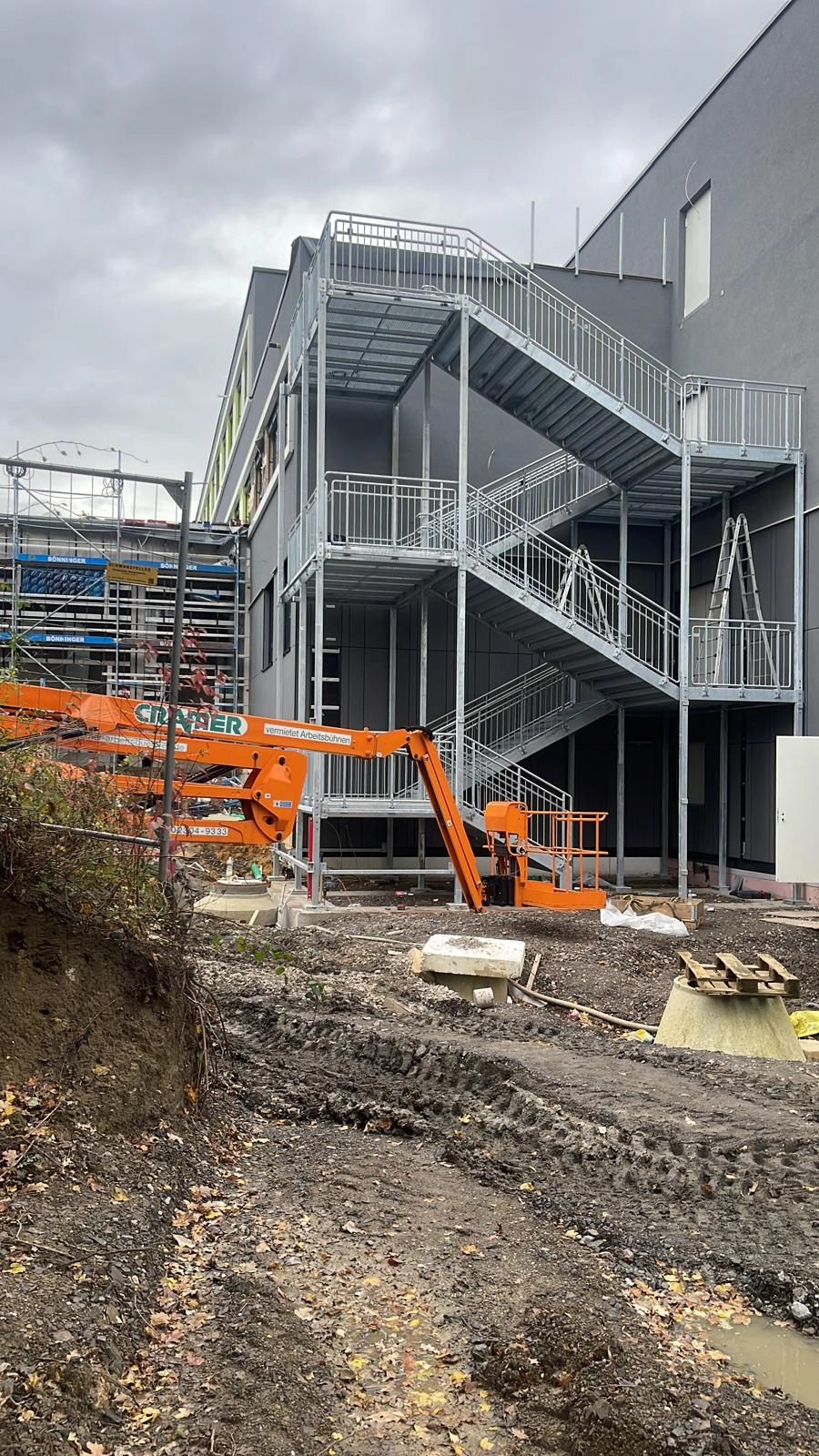 Außentreppen aus Stahl als Fluchttreppe an entstehender Industriehalle mit Baugerät im Vordergrund