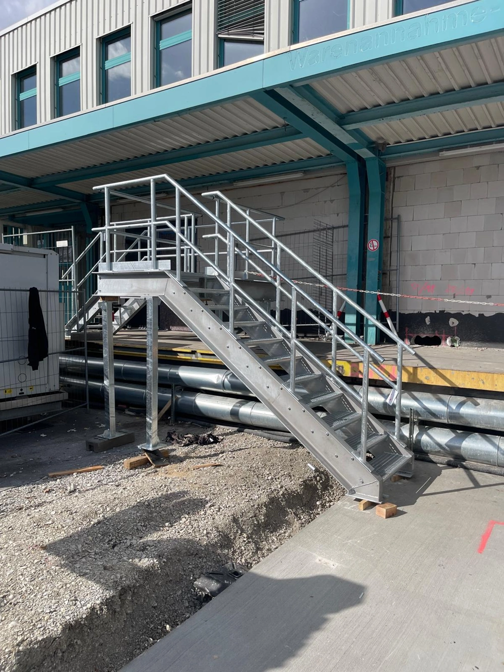 Galvanisierte Metalltreppe mit Treppengeländer auf Baustelle vor Hallenwand – Außentreppen