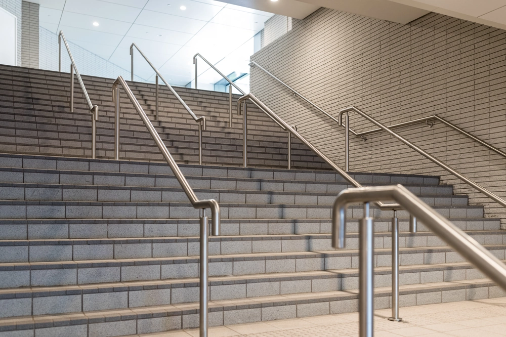 Breite Treppe mit modernem Treppengeländer und Edelstahl-Handlauf in hellem Eingangsbereich