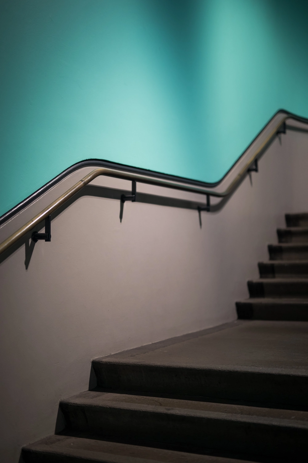 Treppengeländer mit Edelstahlhandlauf an schlichter Betontreppe vor türkiser Wand